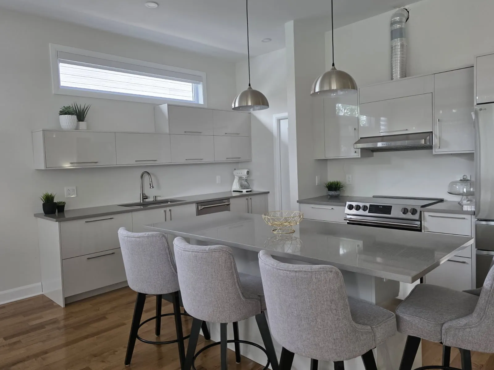 Cuisine RONA moderne blanche à Laval avec îlot en quartz gris, quatre tabourets rembourrés et suspensions