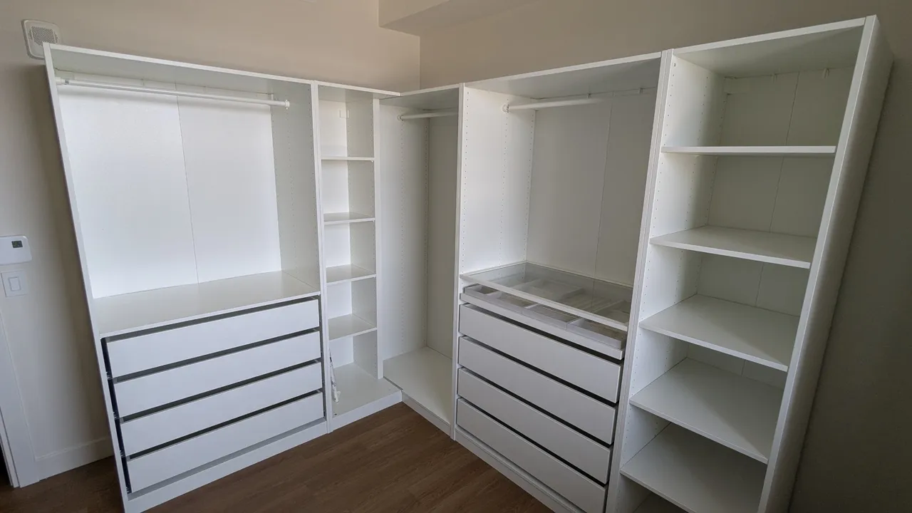 L-shaped IKEA PAX corner wardrobe installed in Laval, with hanging rails, drawer units, a glass-top accessory tray and open shelving