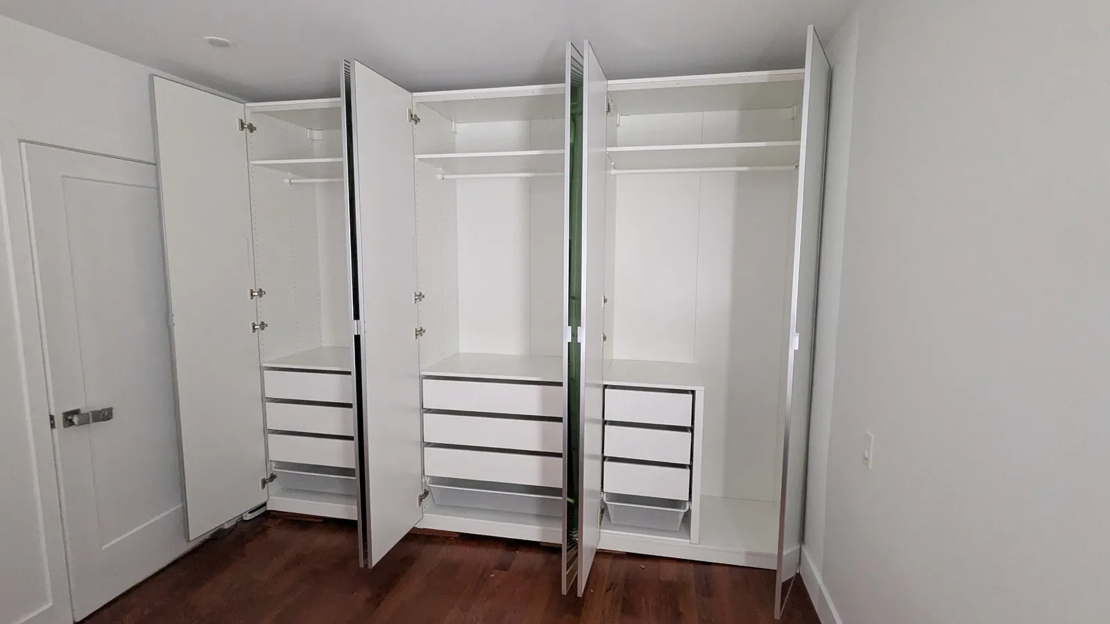 IKEA PAX wardrobe in a bedroom in Sainte-Anne-de-Bellevue with the mirrored doors open, showing hanging rails, shelves and drawers with mesh baskets