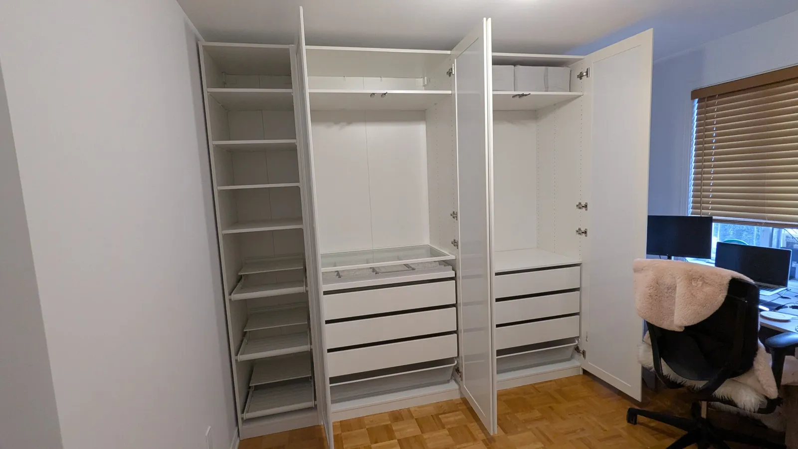 IKEA PAX wardrobe in Saint-Laurent with the doors open, showing a tall unit with pull-out shelves, hanging rails, a glass-top accessory tray, drawers and mesh baskets
