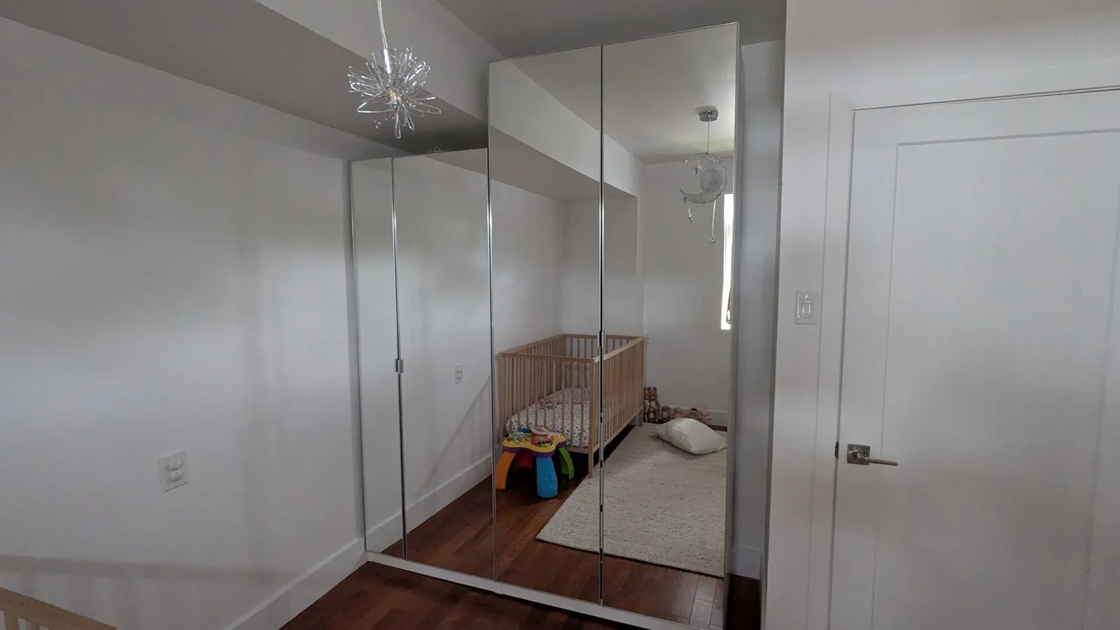 Mirrored IKEA PAX wardrobe doors closed in a child’s bedroom, reflecting a crib