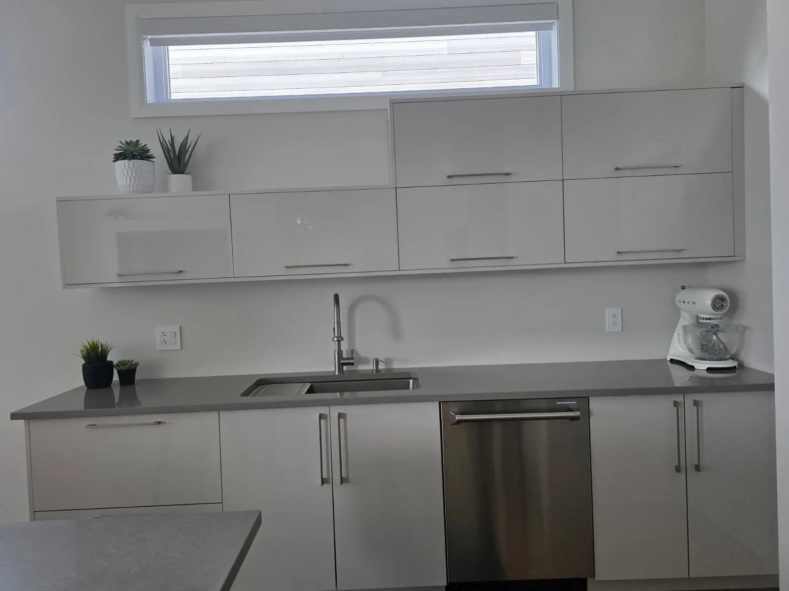 Mur de l’évier d’une cuisine RONA à Laval : armoires hautes brillantes, comptoir en quartz gris et lave-vaisselle en inox