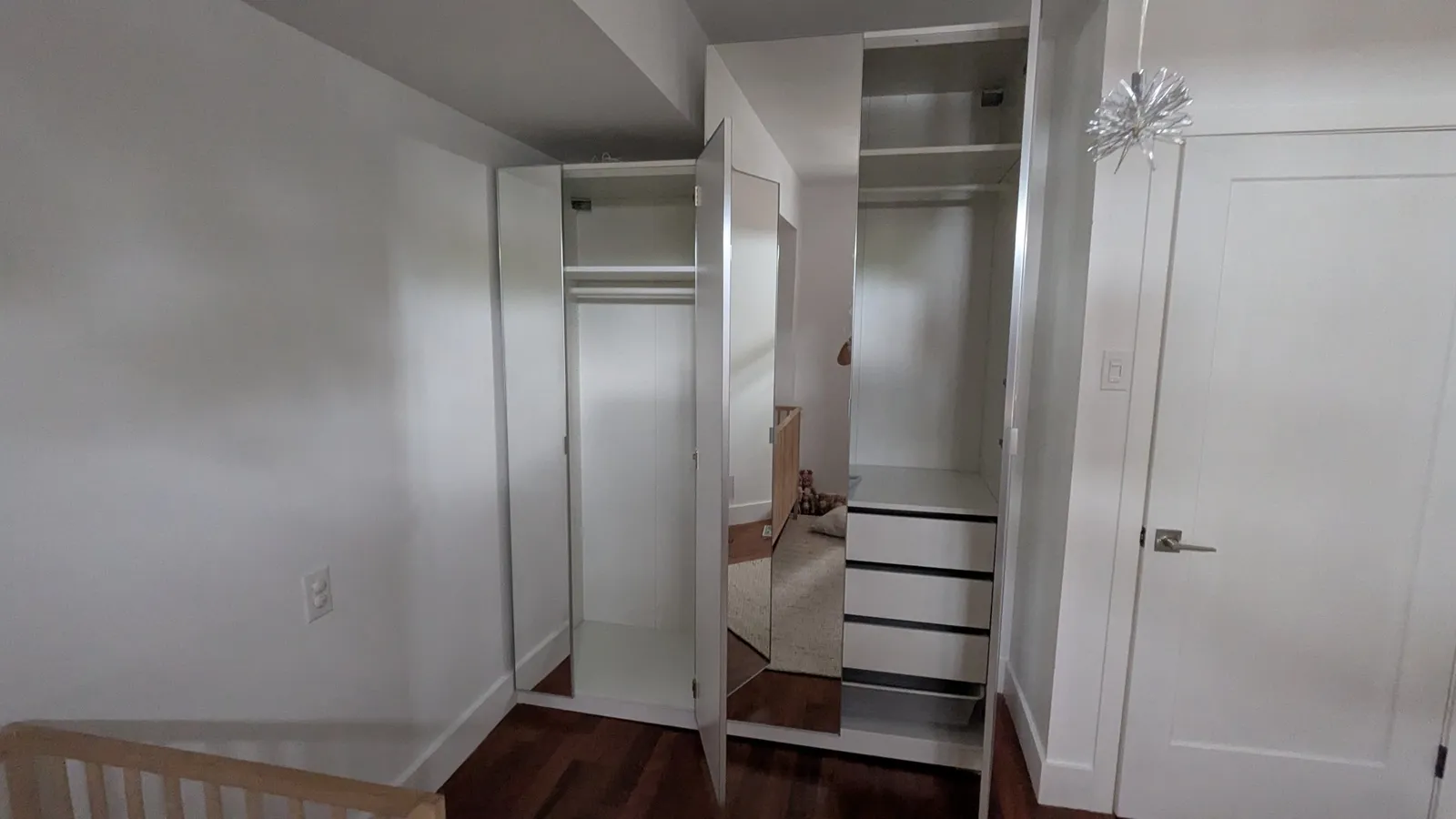 Corner IKEA PAX wardrobe in a child’s bedroom with mirrored doors open, showing a hanging rail, a shelf and drawers with a mesh basket