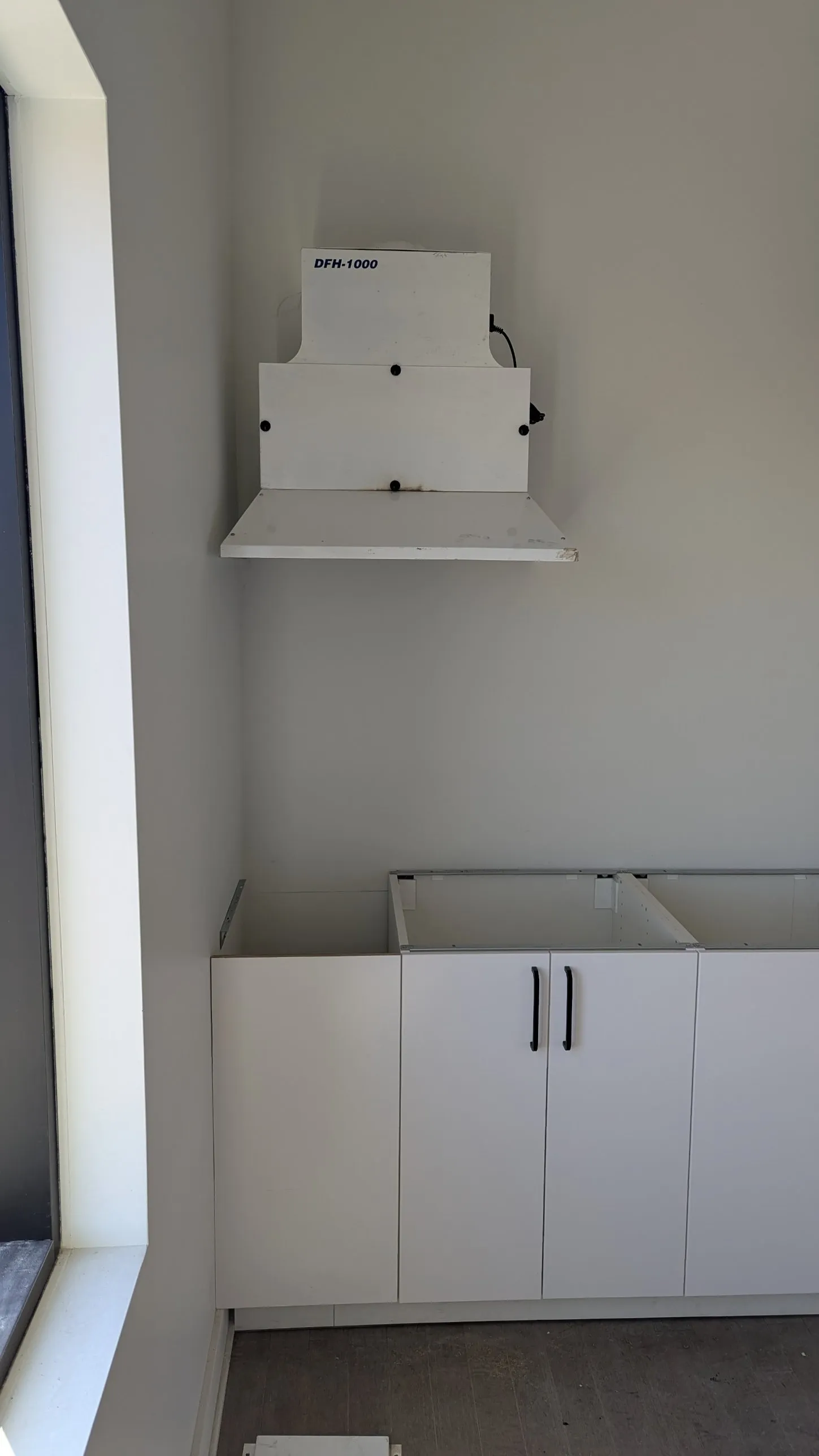 Corner of the IKEA office kitchen with white base cabinets, a wall-mounted unit above and a large window