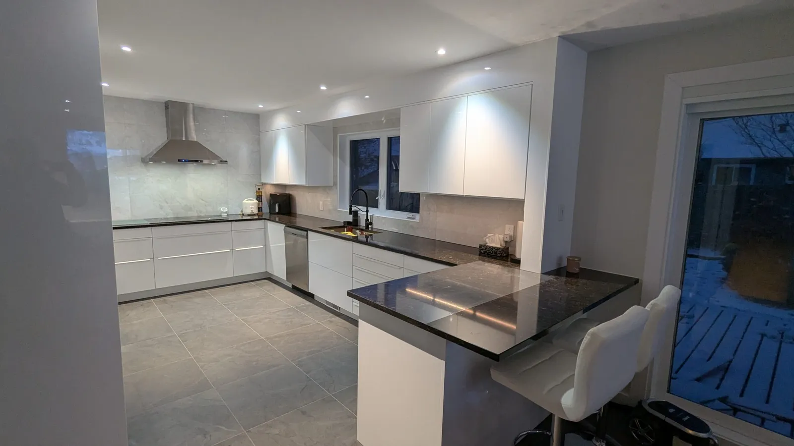 Armoires basses et hautes blanc brillant, hotte en inox et porte-patio dans une cuisine de Kirkland