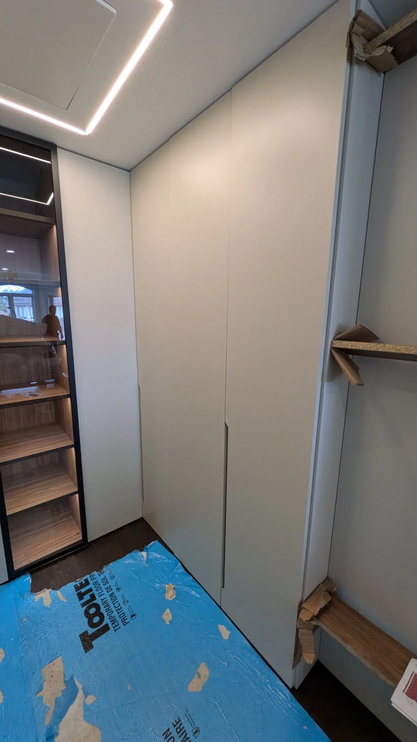 Corner of the custom wardrobe where full-height doors meet a black-framed glass display cabinet with lit walnut shelves