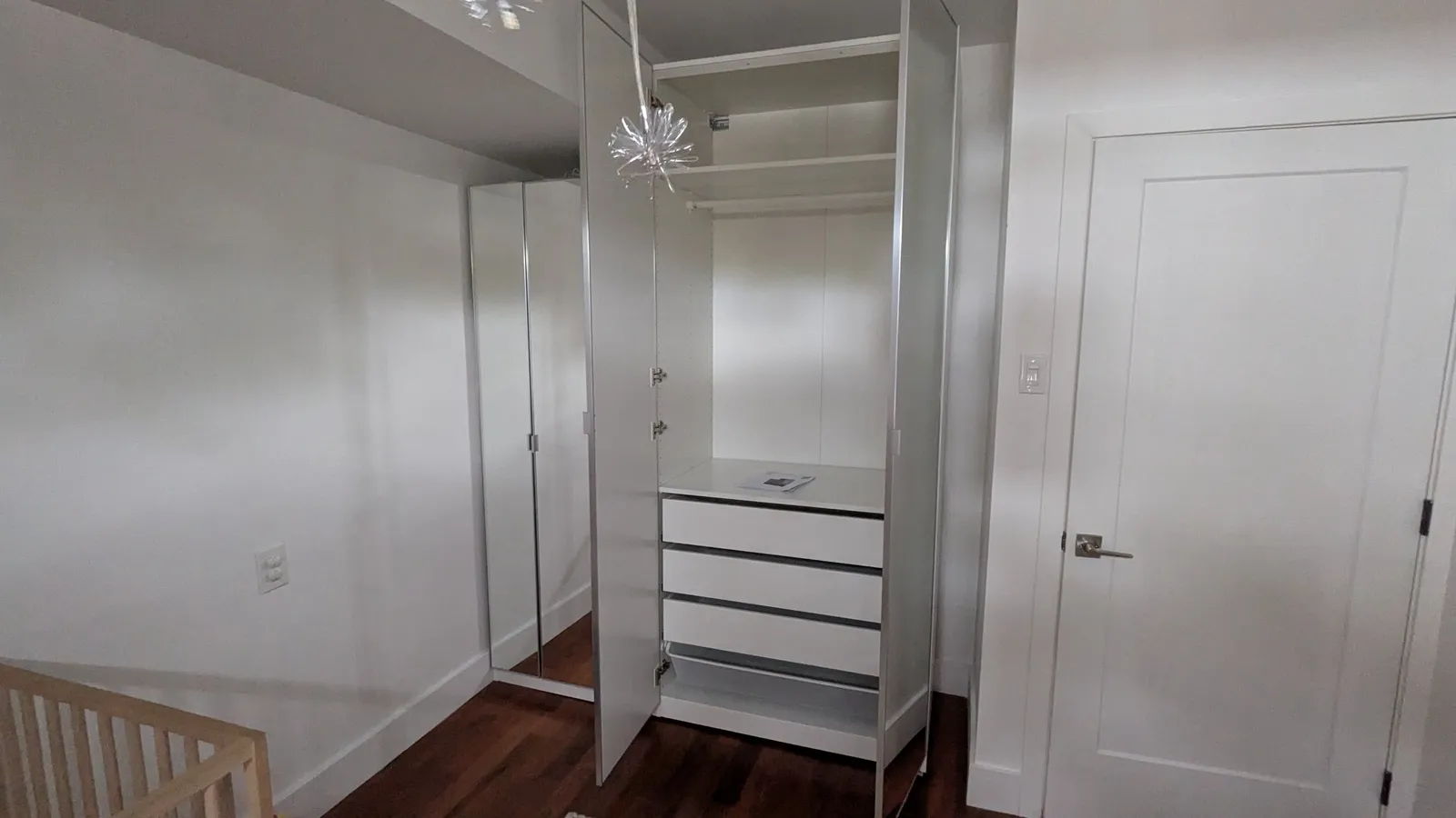 IKEA PAX wardrobe with mirrored doors open, showing a hanging rail, a shelf, three drawers and a mesh basket