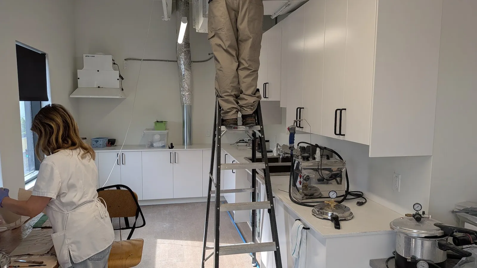 IKEA office kitchen in use by the team, with white cabinets, black bar handles, a countertop with sink and a ventilation unit on the wall