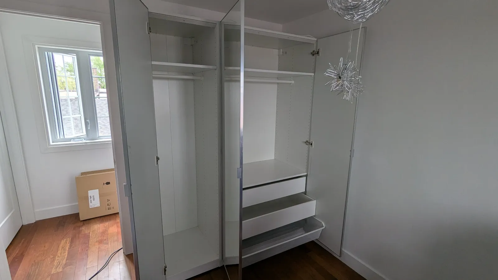 Two IKEA PAX wardrobes with mirrored doors open in a third room, with hanging rails, shelves and drawers