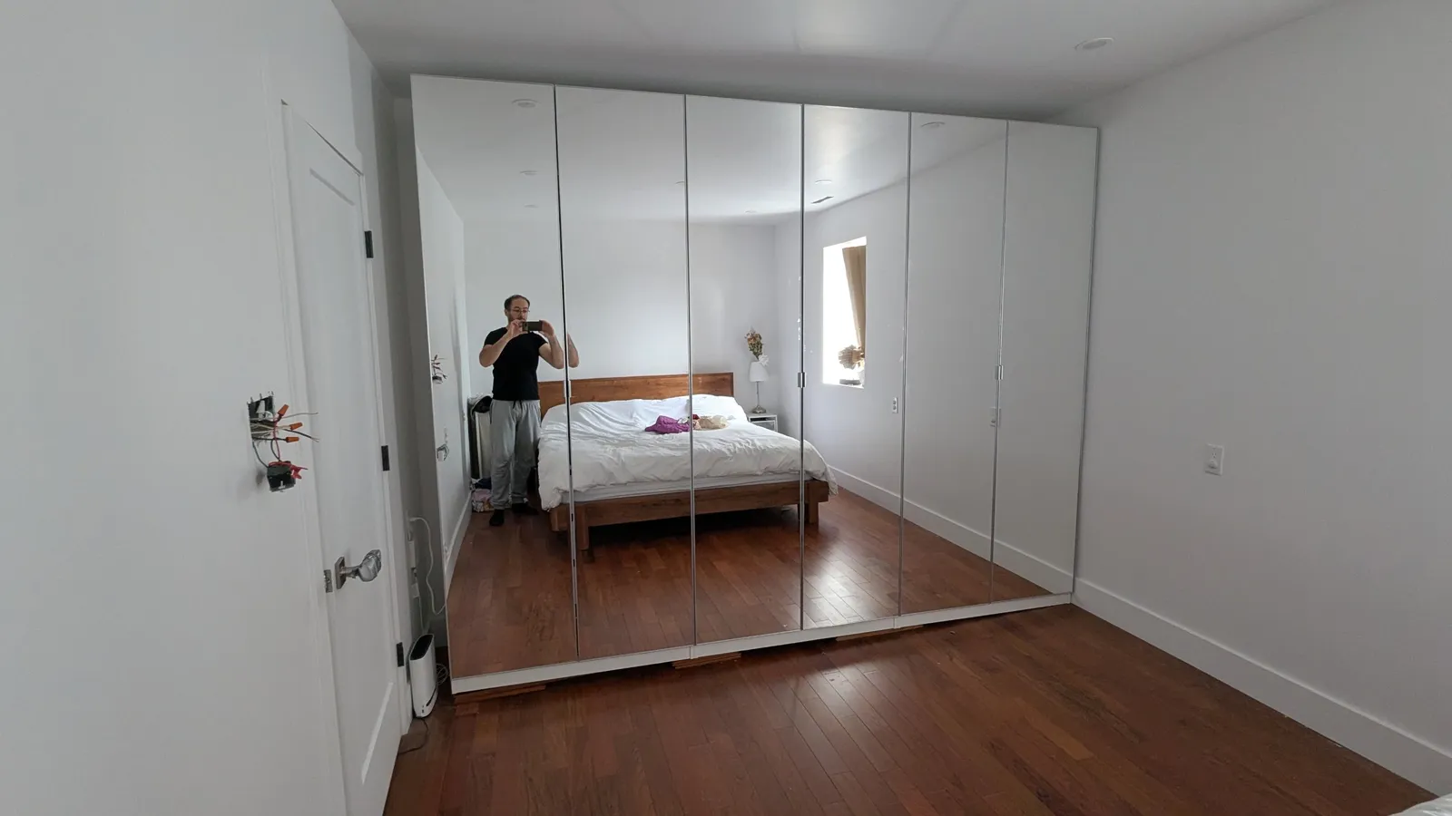 Run of mirrored IKEA PAX wardrobe doors closed along a bedroom wall, reflecting the room