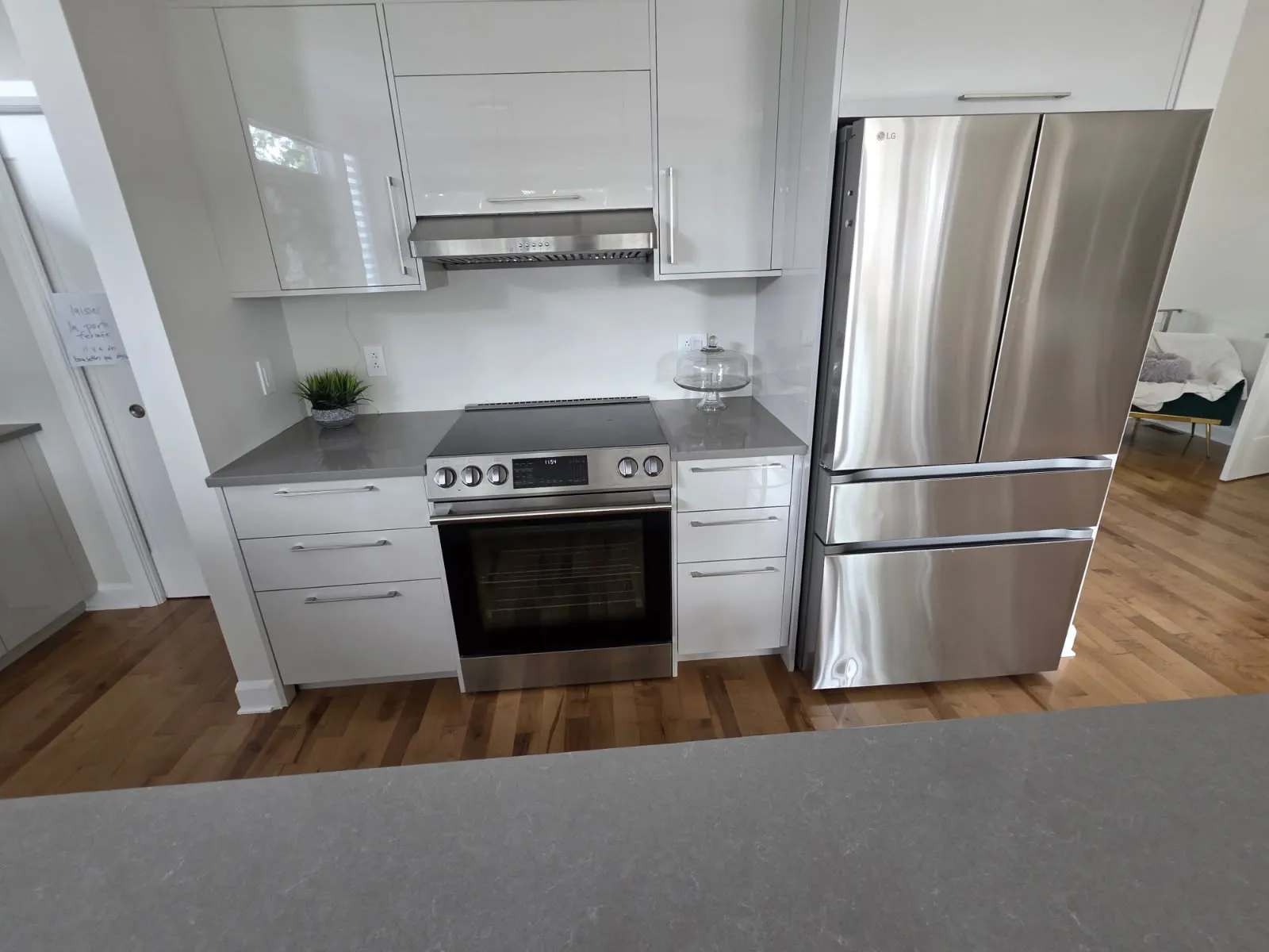 Coin cuisson avec cuisinière électrique, hotte et réfrigérateur à côté d’armoires claires, cuisine de Laval